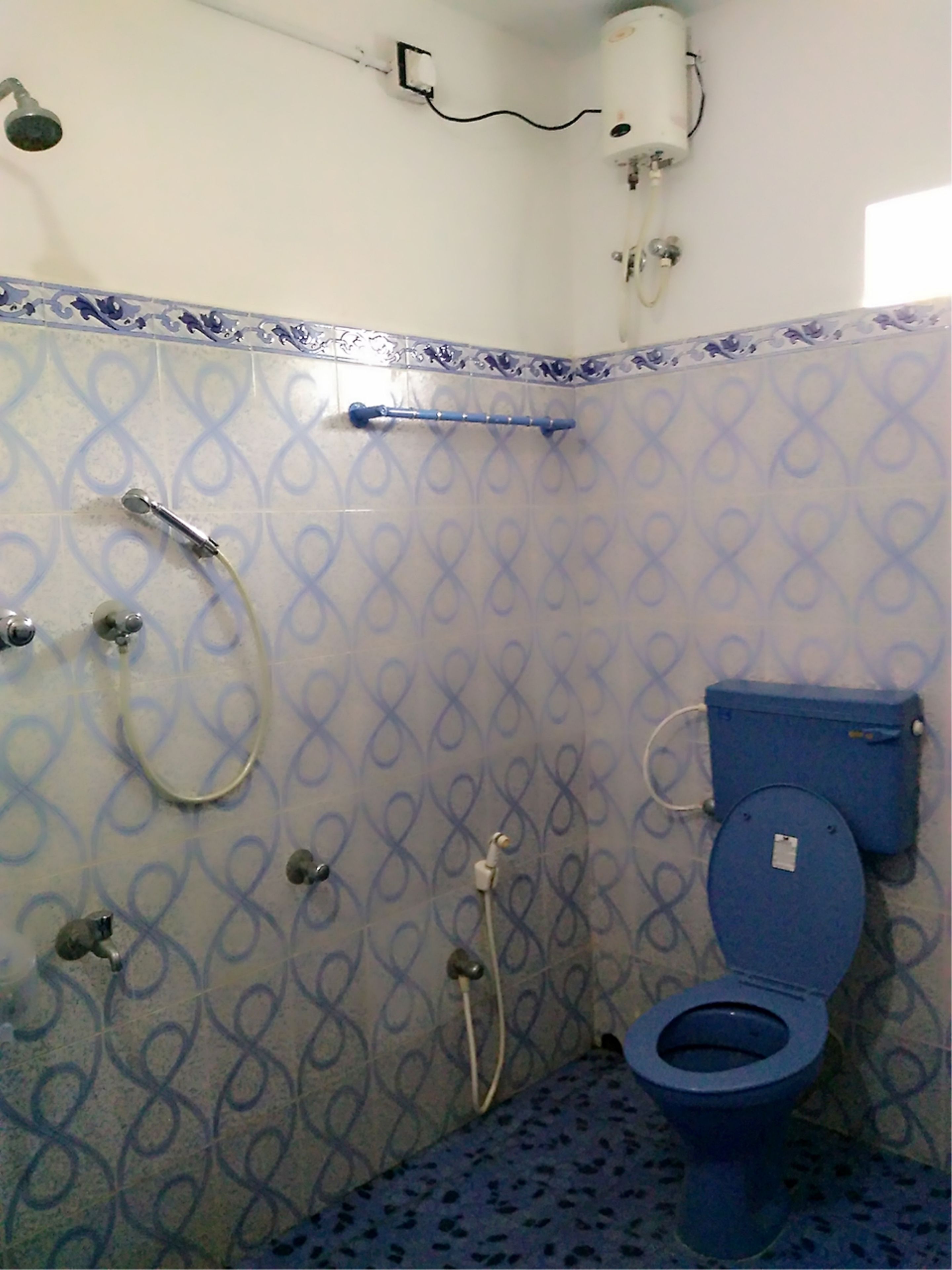 A bathroom with a patterned tile wall, a shower, a toilet, and a towel rack.