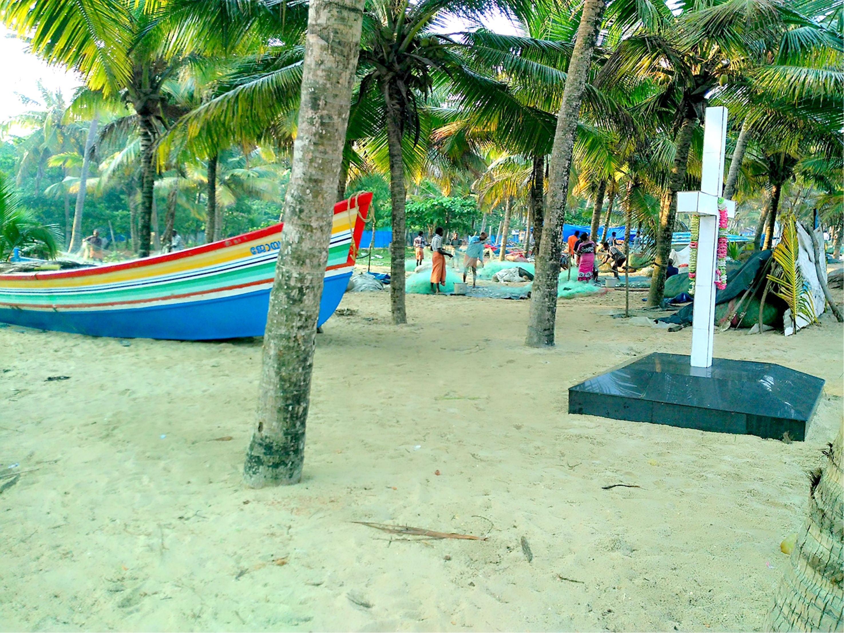 Una spiaggia con una barca colorata, palme e un monumento a forma di croce.