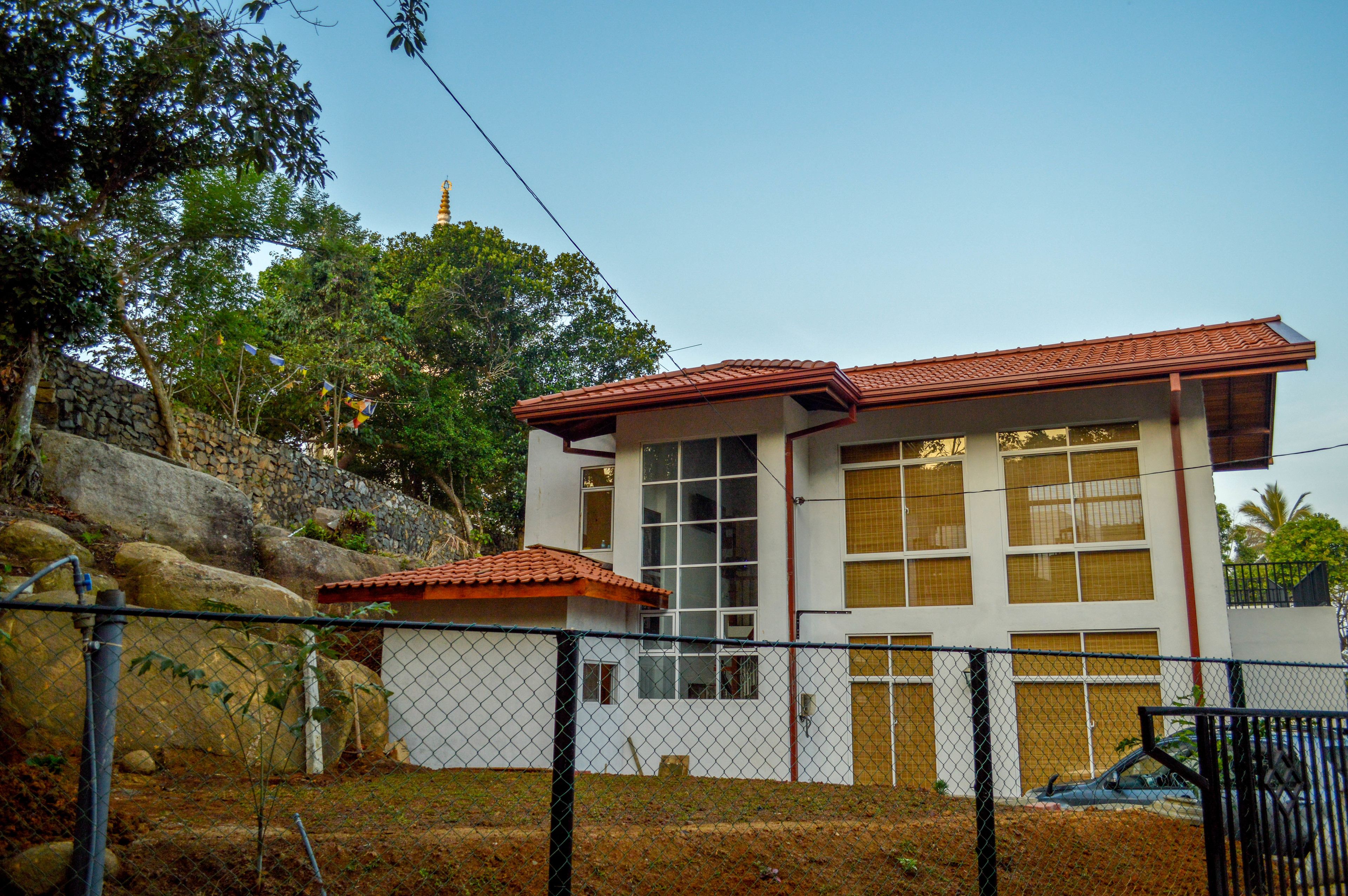 A two-story building with a red-tiled roof, large windows, and a stone wall.