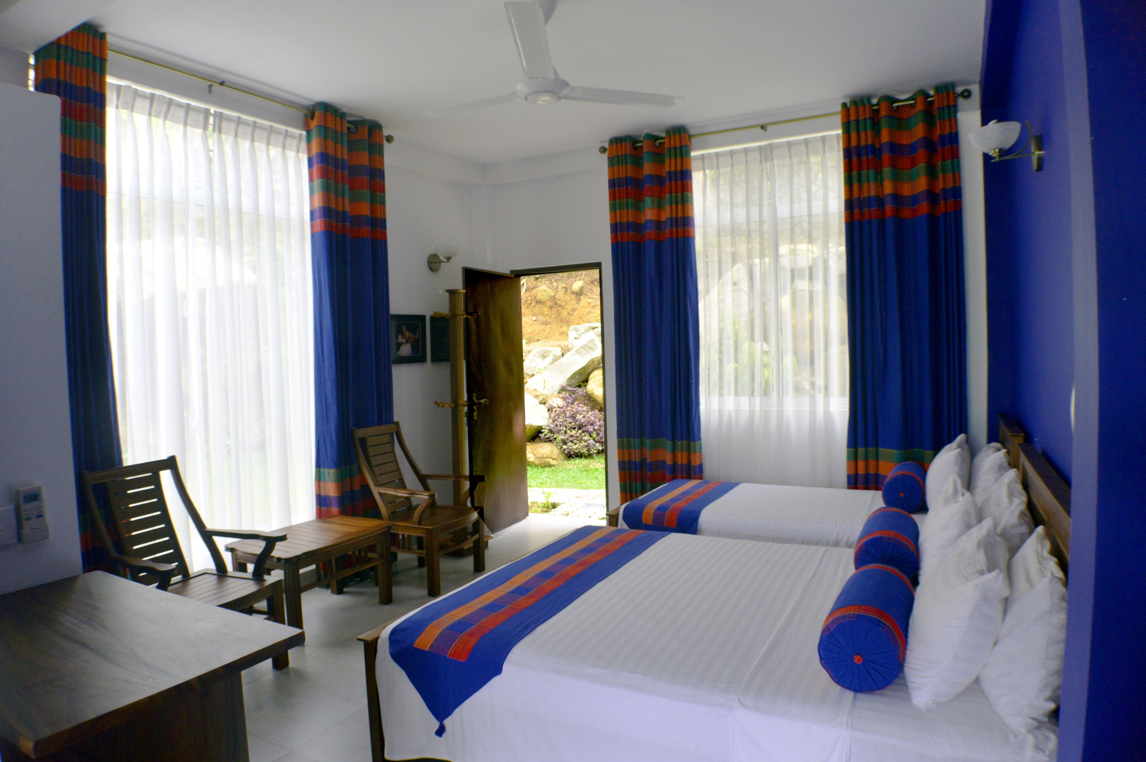 A hotel room with two beds, a dining table, chairs, and a view of the outdoors.