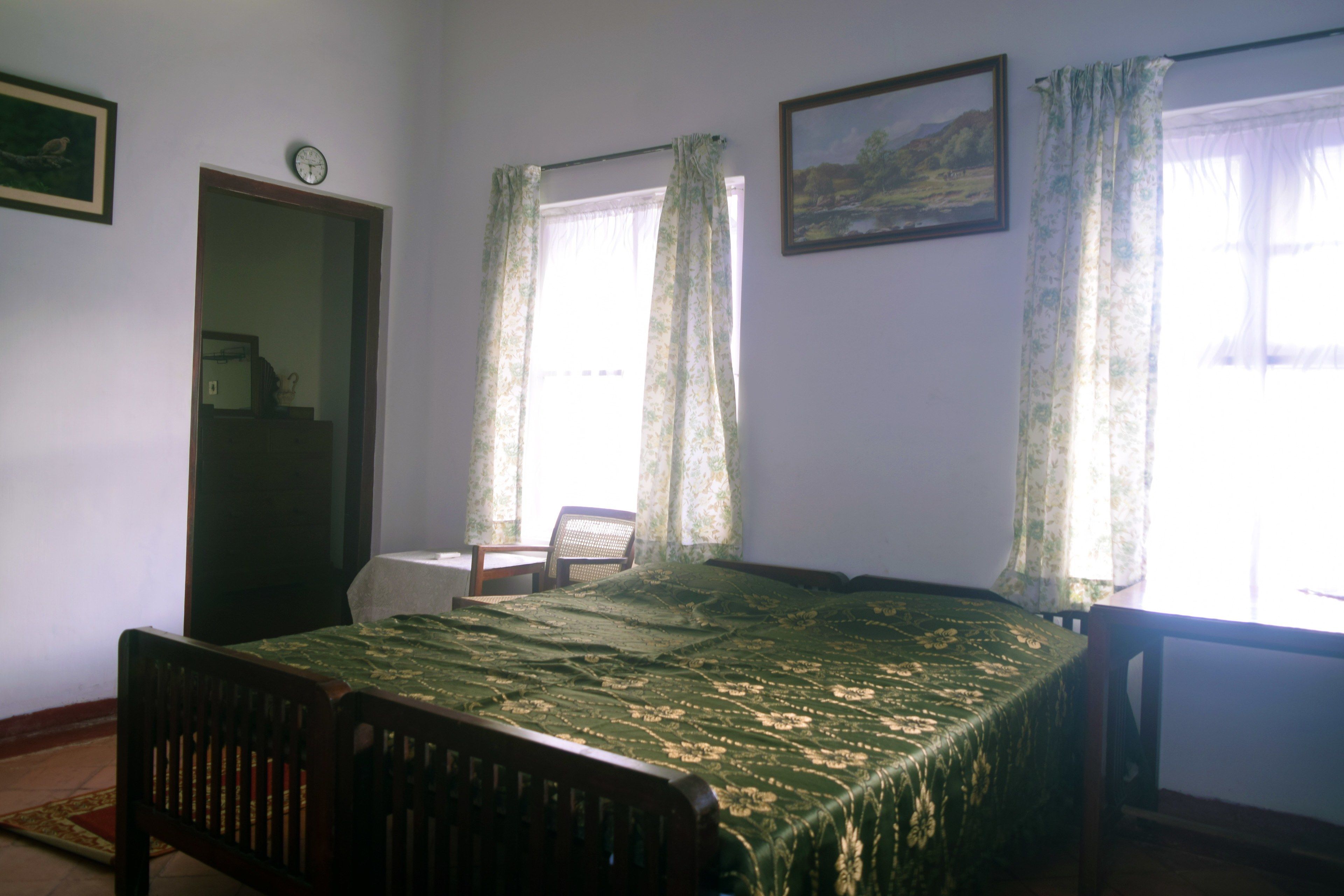 Un dormitorio con cama, una silla, un escritorio y una ventana con cortinas.