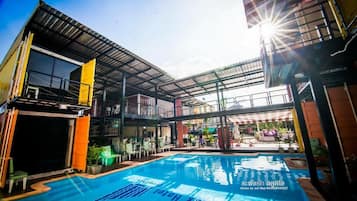 Un hotel moderno con zona de piscina, mobiliario exterior y un patio cubierto.