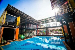 A modern hotel with a pool area, outdoor seating, and a covered patio.