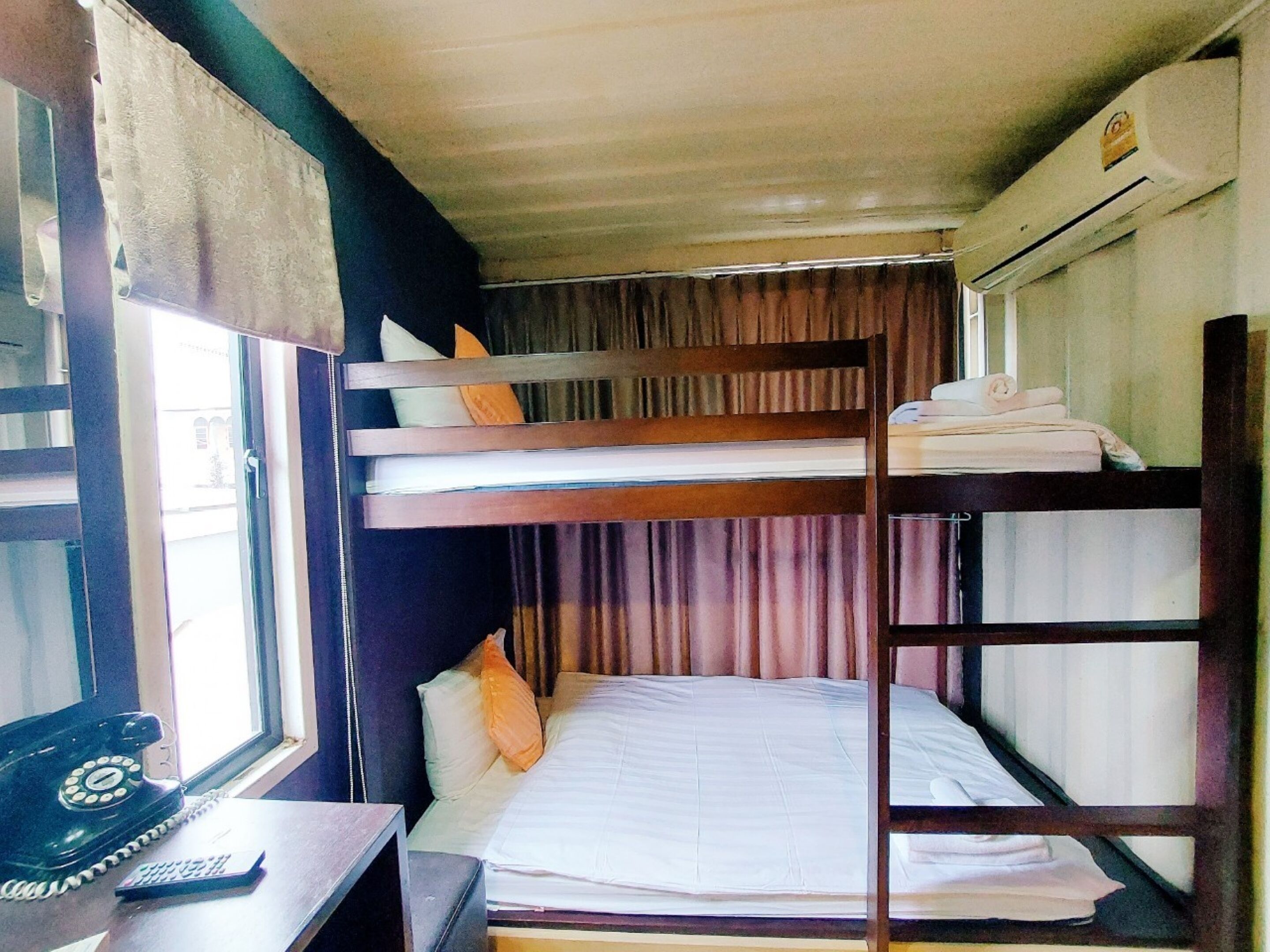 Een slaapkamer met stapelbed, bureau, telefoon en een airconditioning.