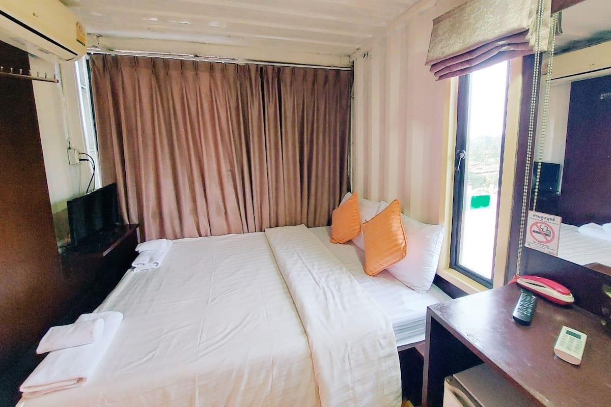 Habitación de hotel con cama, escritorio con teléfono, televisión y ventana con cortinas.