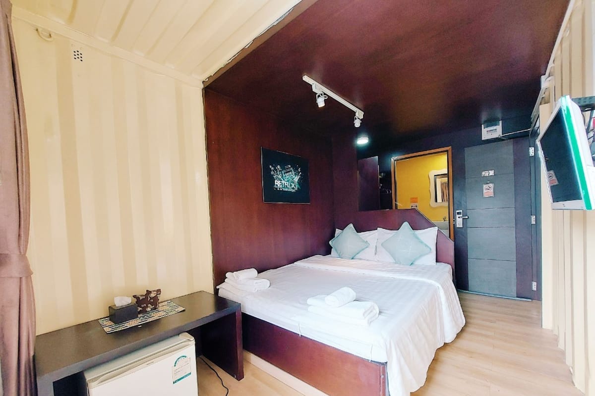 Una habitación de hotel con cama, mesita de noche y un escritorio pequeño con refrigerador.