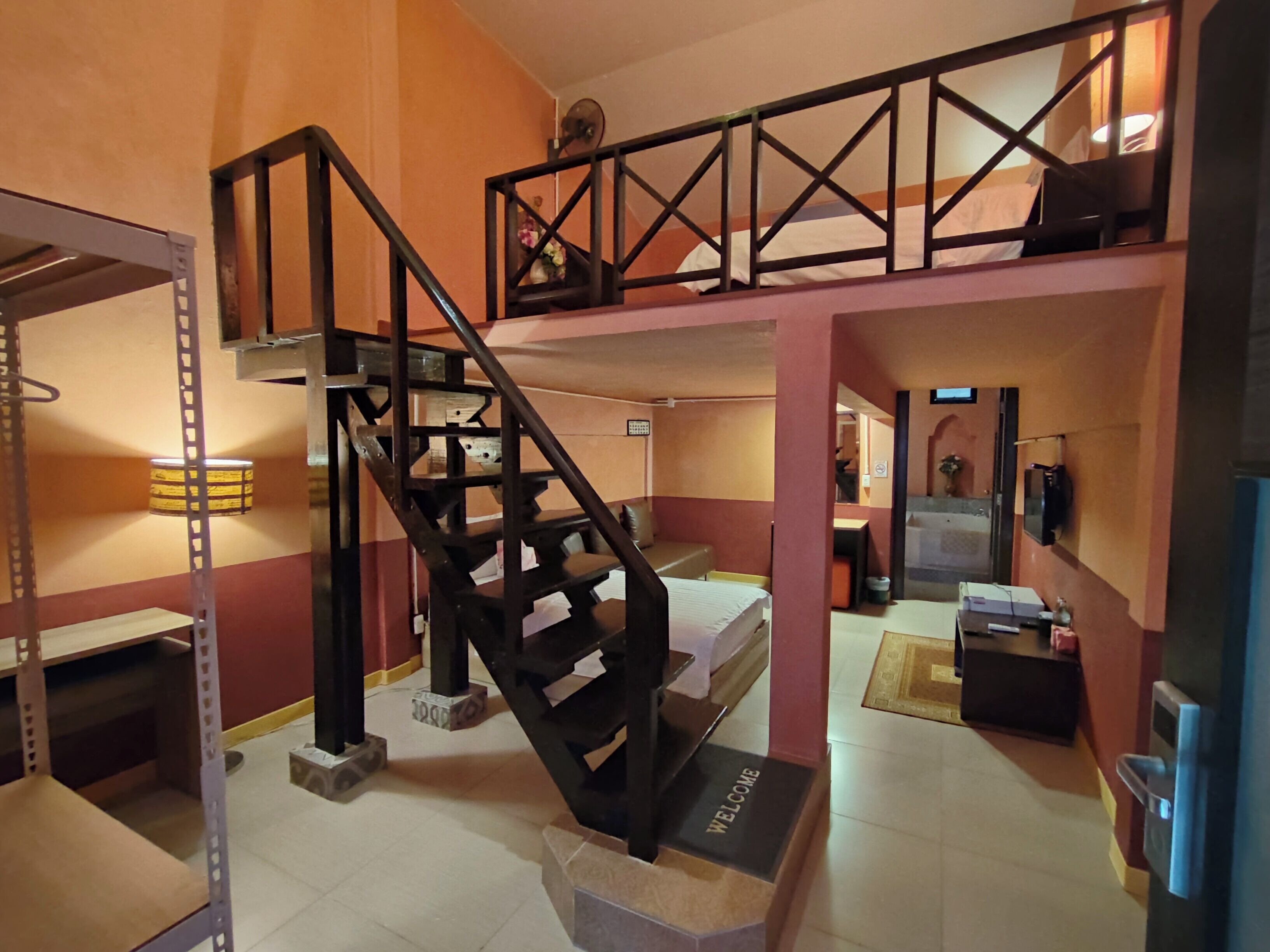 A multi-level room with a black metal staircase, a welcome mat, and a bed.