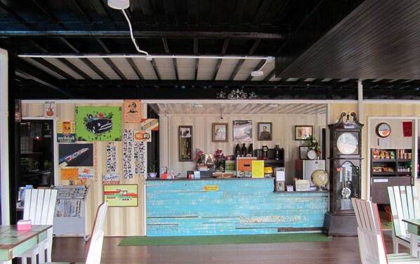 Pequeña tienda rústica con un mostrador azul, varios letreros y un reloj en la pared.