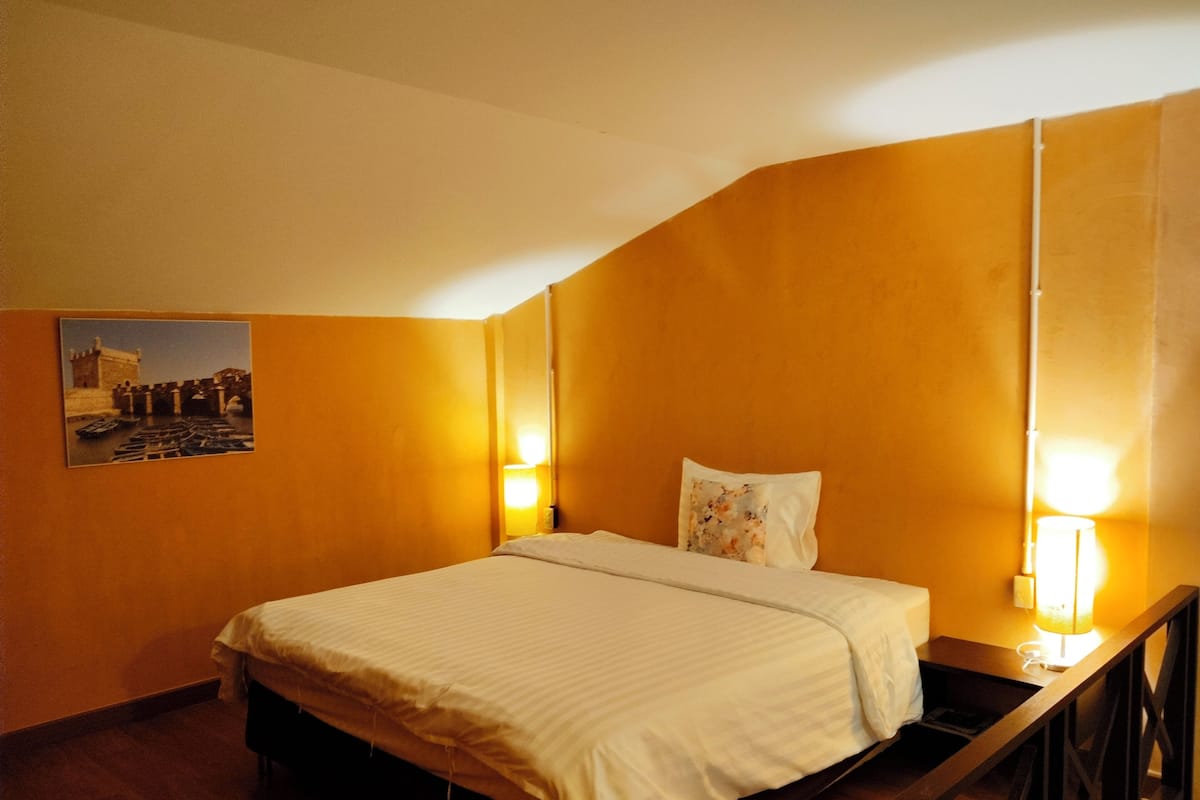 Una habitación de hotel con una cama, una mesita de noche, una lámpara y un cuadro colgado en la pared.