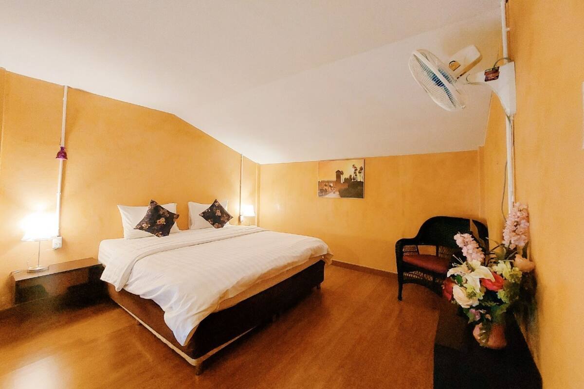 Habitación de hotel con cama, una silla, mesita de noche, lámpara y aire acondicionado instalado en la pared.