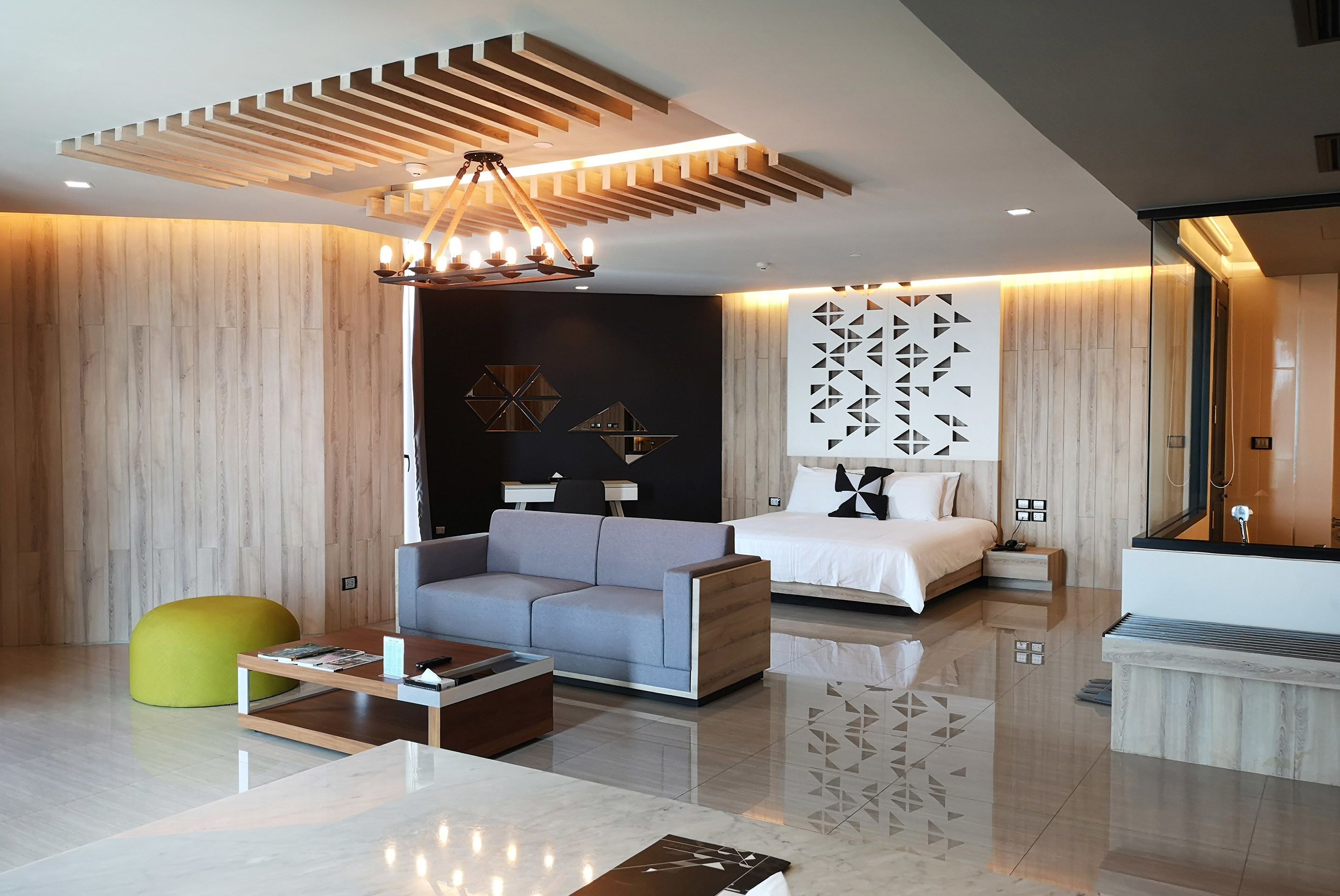 Une chambre d’hôtel moderne avec un canapé, un lit, une petite table et un pouf jaune.