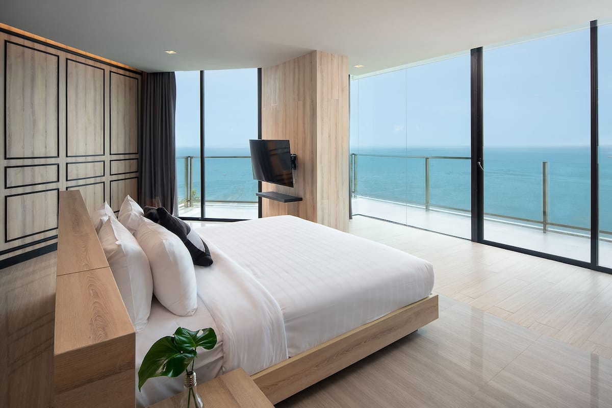 Une chambre moderne avec un grand lit, une tête de lit en bois et une vue sur l’océan.