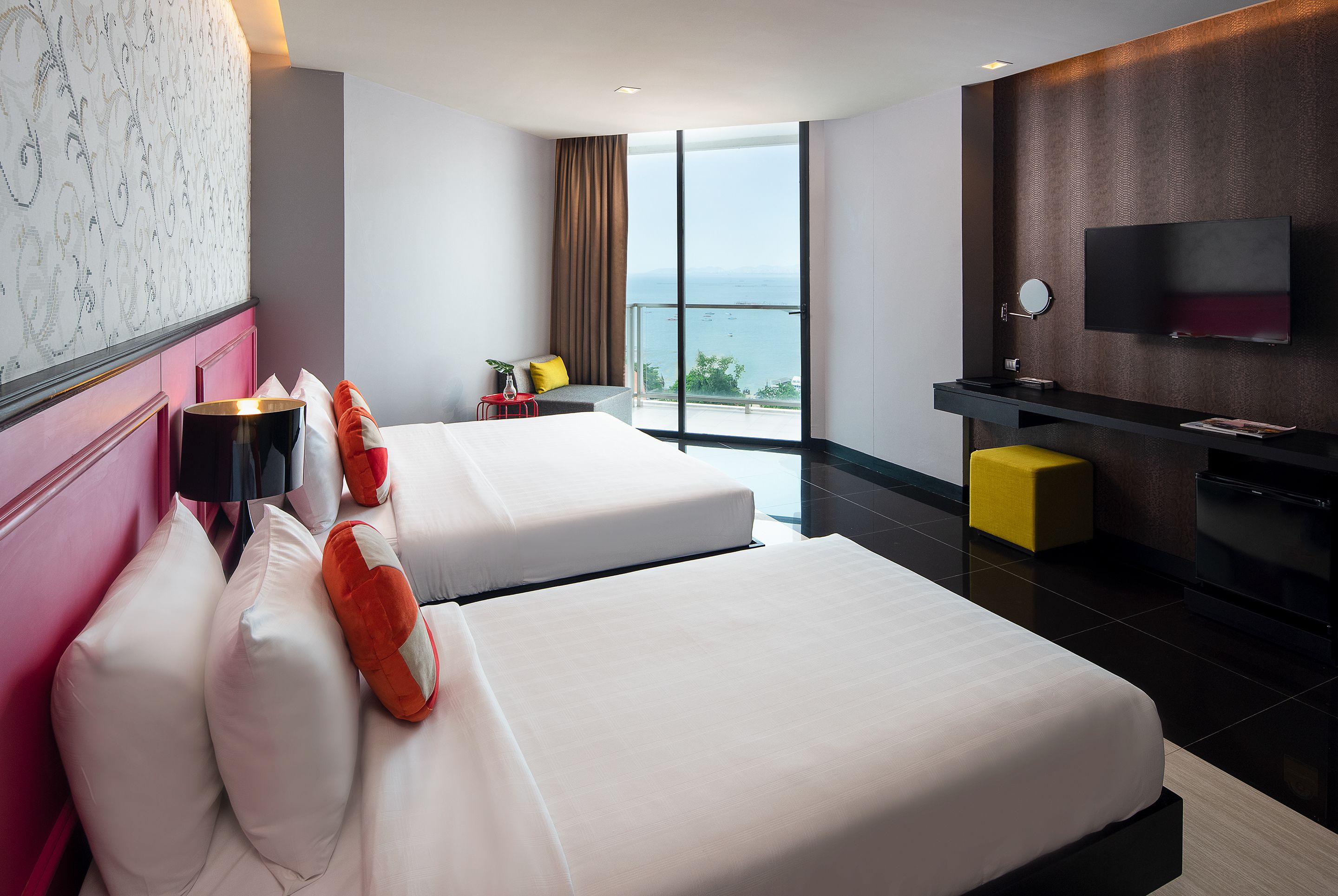 A hotel room with two beds, a TV, a small table, and a view of the sea.