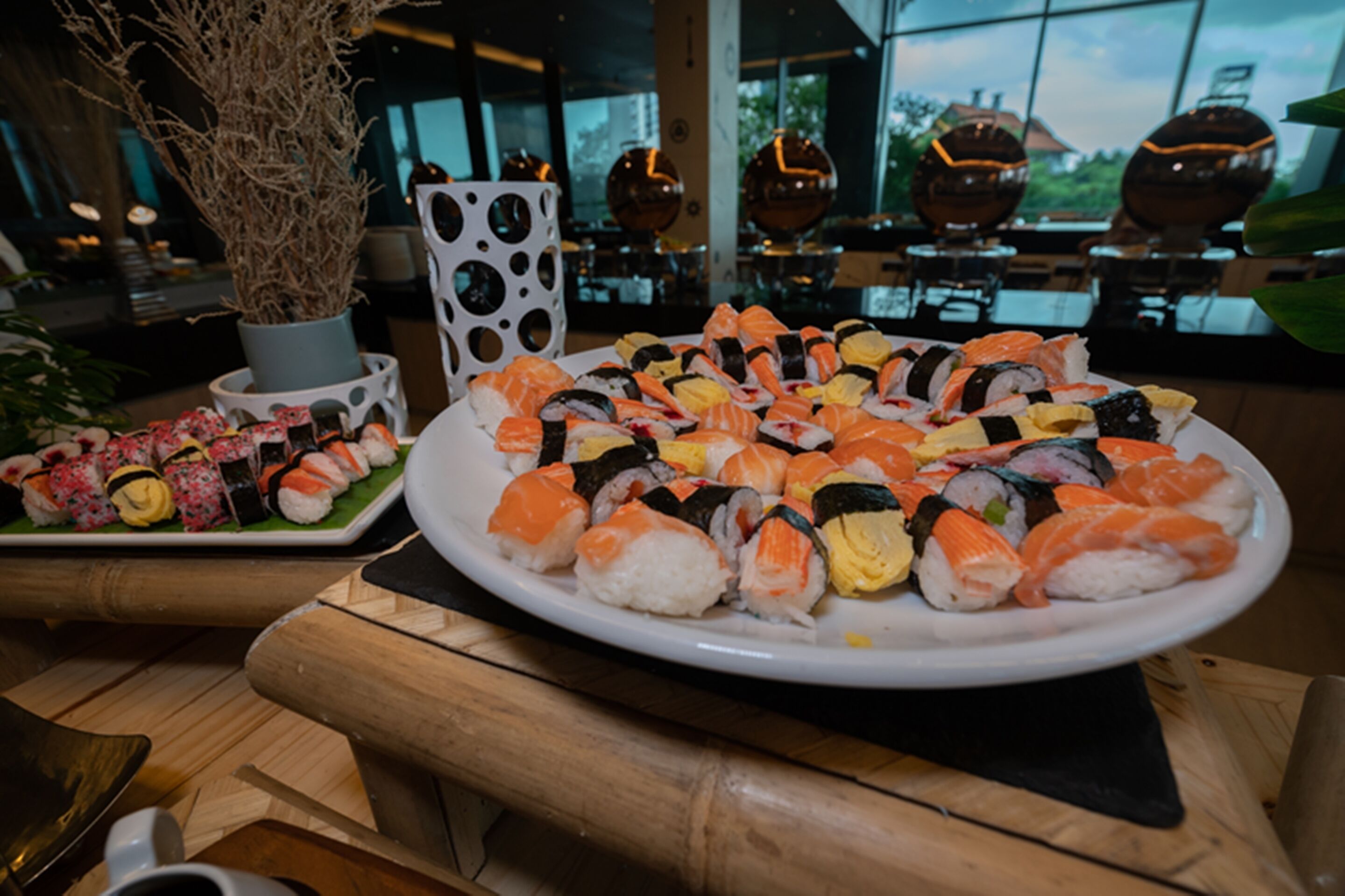 A sushi platter on a wooden table in a restaurant with a large window in the background.