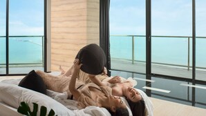 Une chambre d’hôtel moderne dotée d’une grande fenêtre donnant sur un balcon avec vue sur la mer.