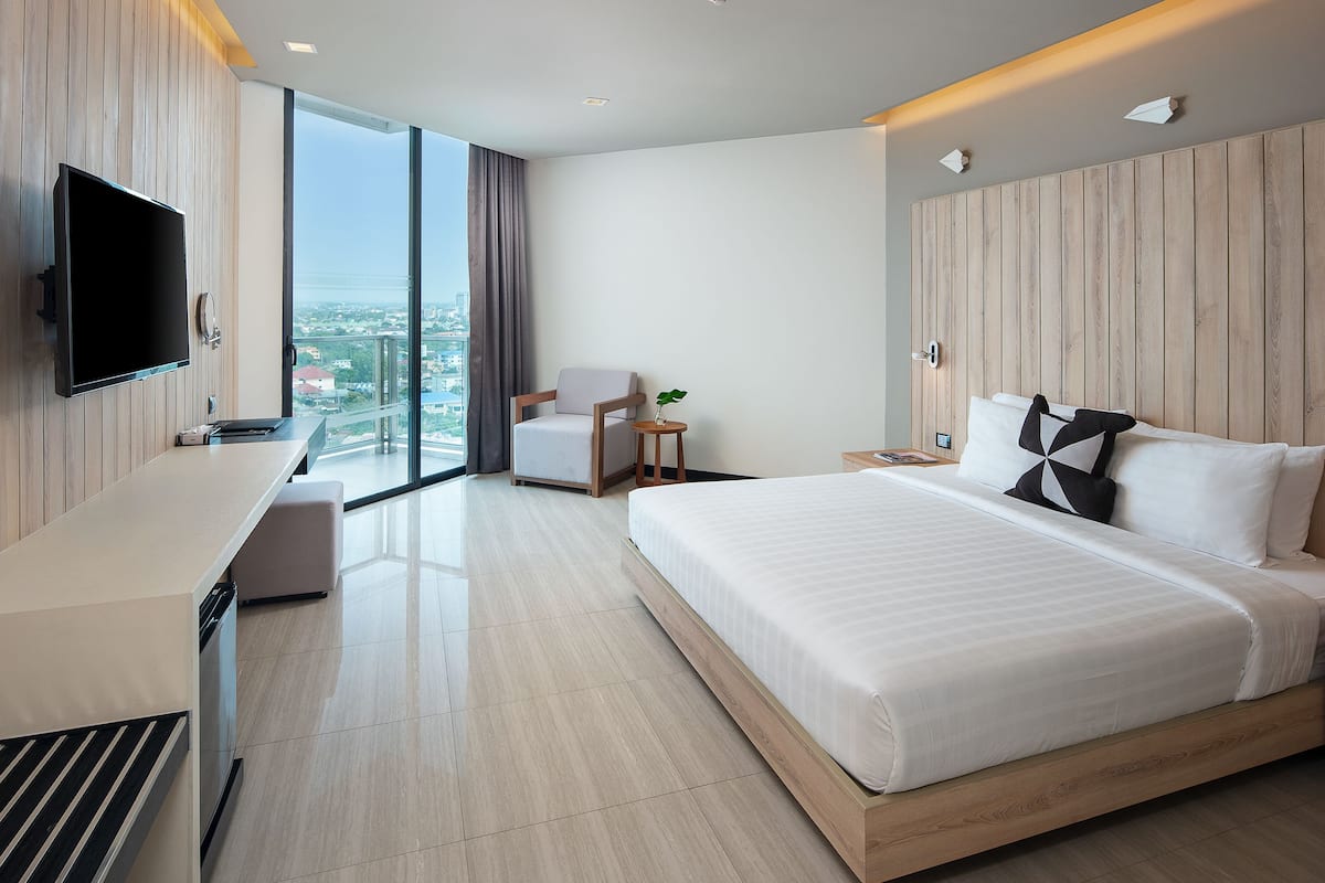 Une chambre d’hôtel moderne dotée d’un grand lit, d’un téléviseur fixé au mur, d’un bureau avec une chaise et offrant une vue sur la ville grâce à de grandes fenêtres.
