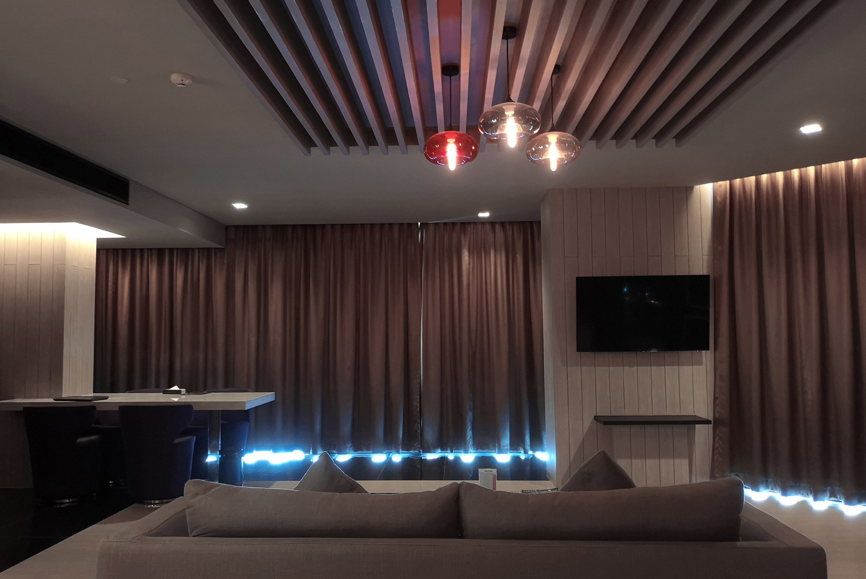 A modern living room with a sofa, a TV mounted on the wall, and a ceiling with a unique design.