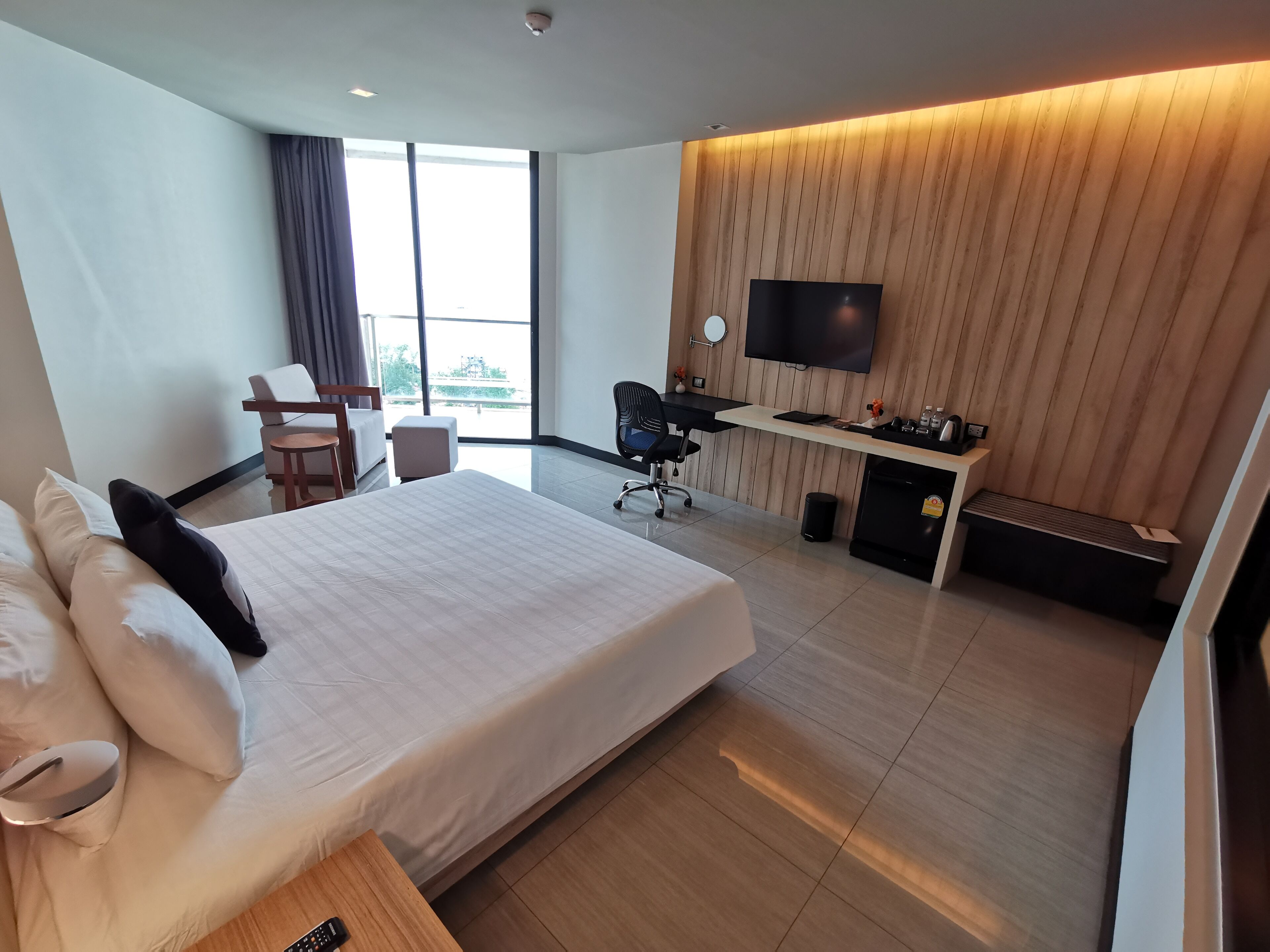 A hotel room with a large bed, a desk, a chair, a TV, and a view through the window.
