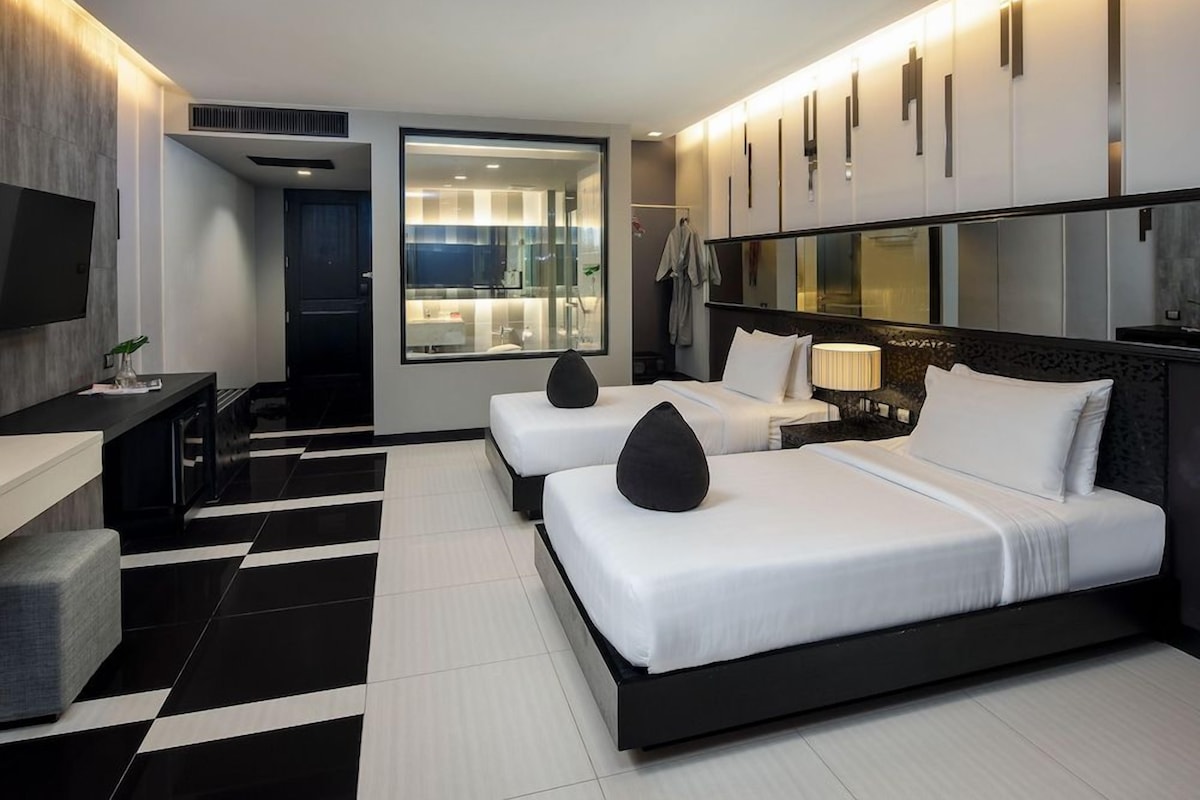 A hotel room with two beds, a TV, a desk, and a large window.