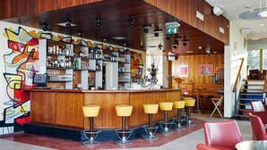 A bar area with wooden paneling, a counter with stools, and a variety of bottles and glasses. - Pension Homeland (Amsterdam)