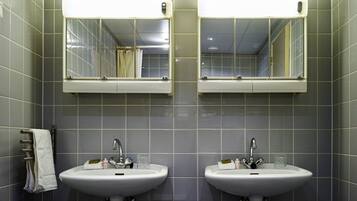 Une salle de bain avec deux lavabos, chacun étant surmonté d’un miroir. Des serviettes sont suspendues sur un porte-serviettes situé à gauche.