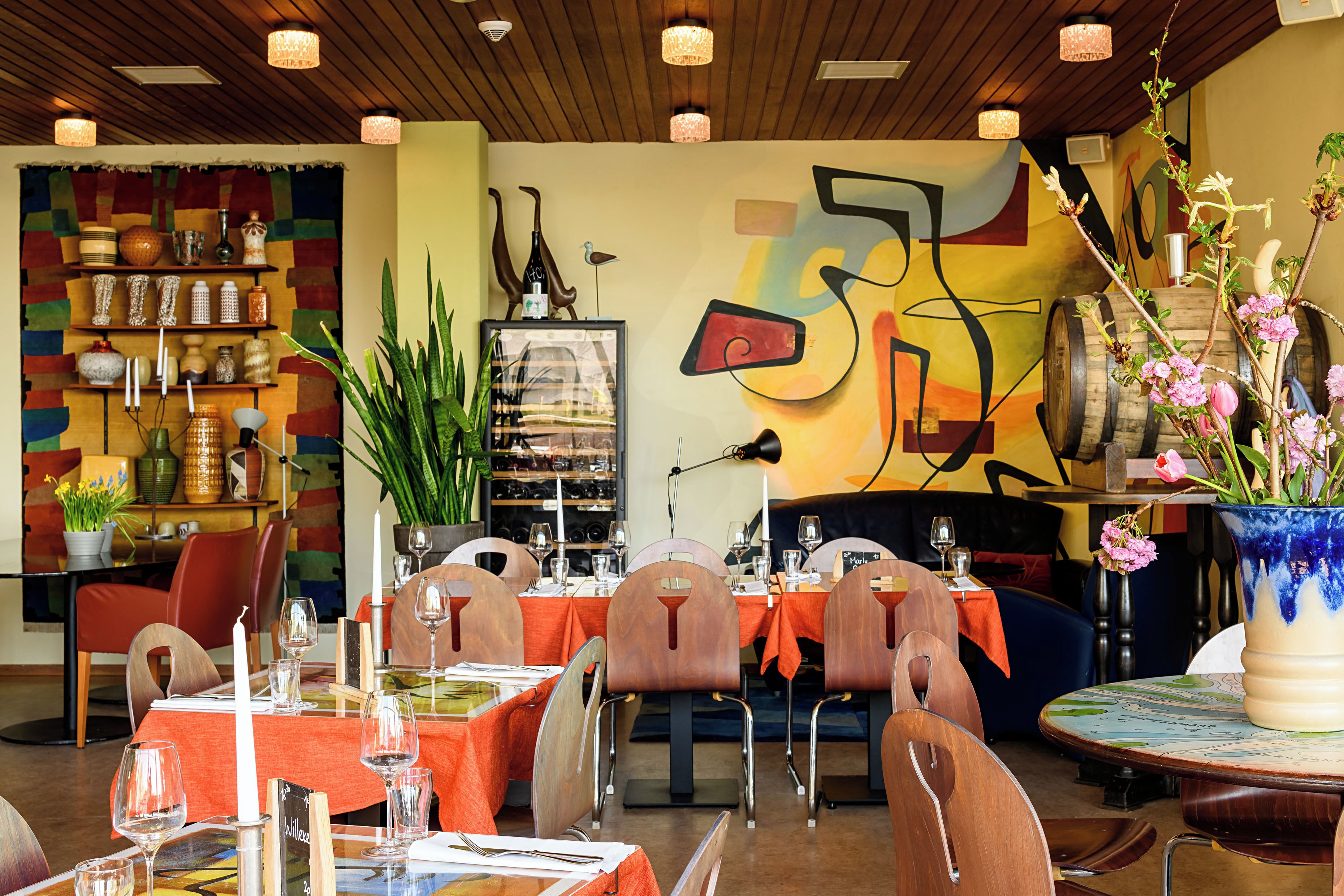 A restaurant interior with tables set for dining, a variety of decorative items, and a colorful abstract mural on the wall.