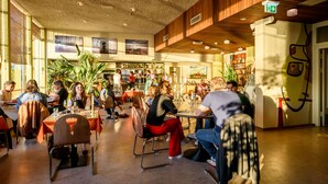 A spacious indoor dining area with multiple tables and chairs, wooden paneling on the walls, and large windows allowing natural light. - Pension Homeland (Amsterdam)