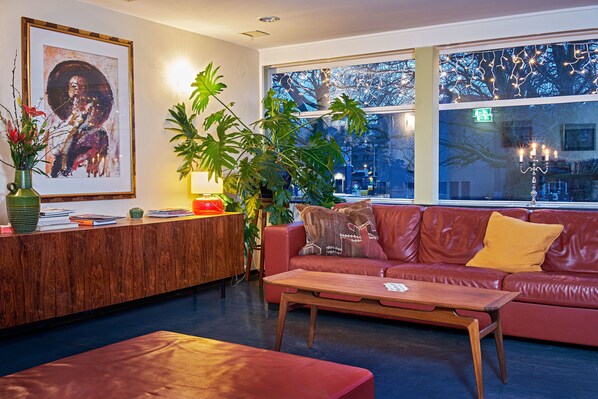 A modern living room with a red leather sofa, a wooden coffee table, and a large window with a view of trees. - Pension Homeland (Amsterdam)