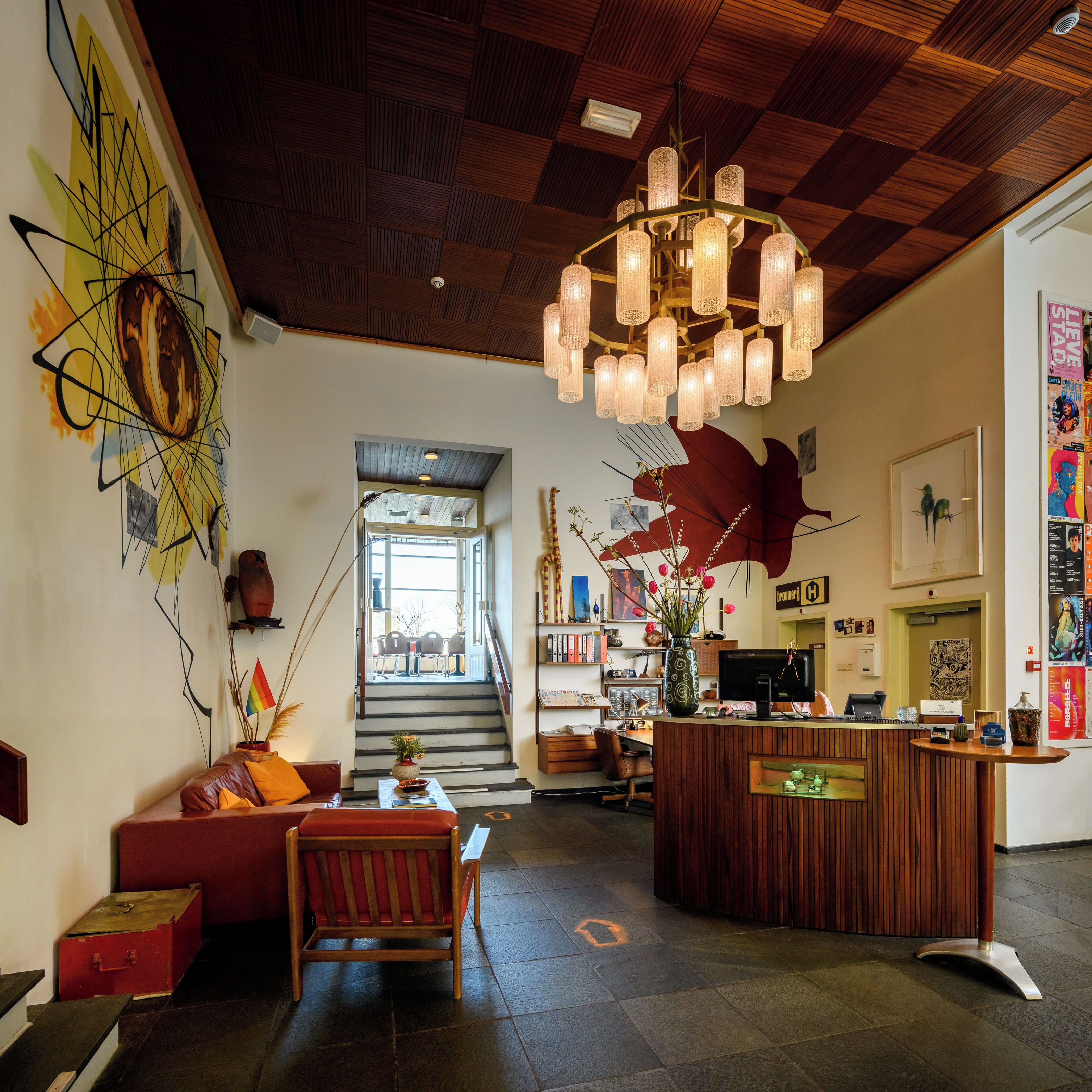 Amplia sala de estar con techo de madera, un candelabro central, un sofá rojo, una mesa de centro de madera y una escalera que conduce a un nivel superior.