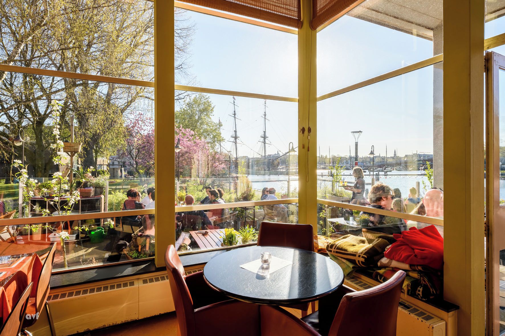 Un restaurante con vista a un río y un barco, con mesas y sillas redondas.