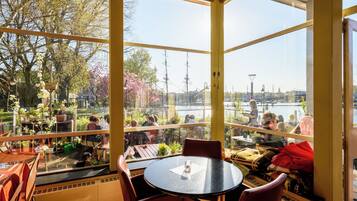 Un restaurante con vista a un río y un barco, con mesas y sillas redondas.