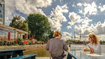 Een café aan de rivier met terras, uitzicht op het water en een historisch schip op de achtergrond.