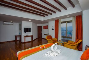 Une chambre d’hôtel comprenant un lit, une télévision, une fenêtre avec des rideaux, une chaise, une petite table et un climatiseur fixé au mur.