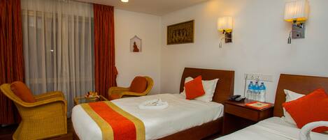 A hotel room with two beds, a wooden headboard, a nightstand, a chair, a window with curtains, and wall-mounted lamps.