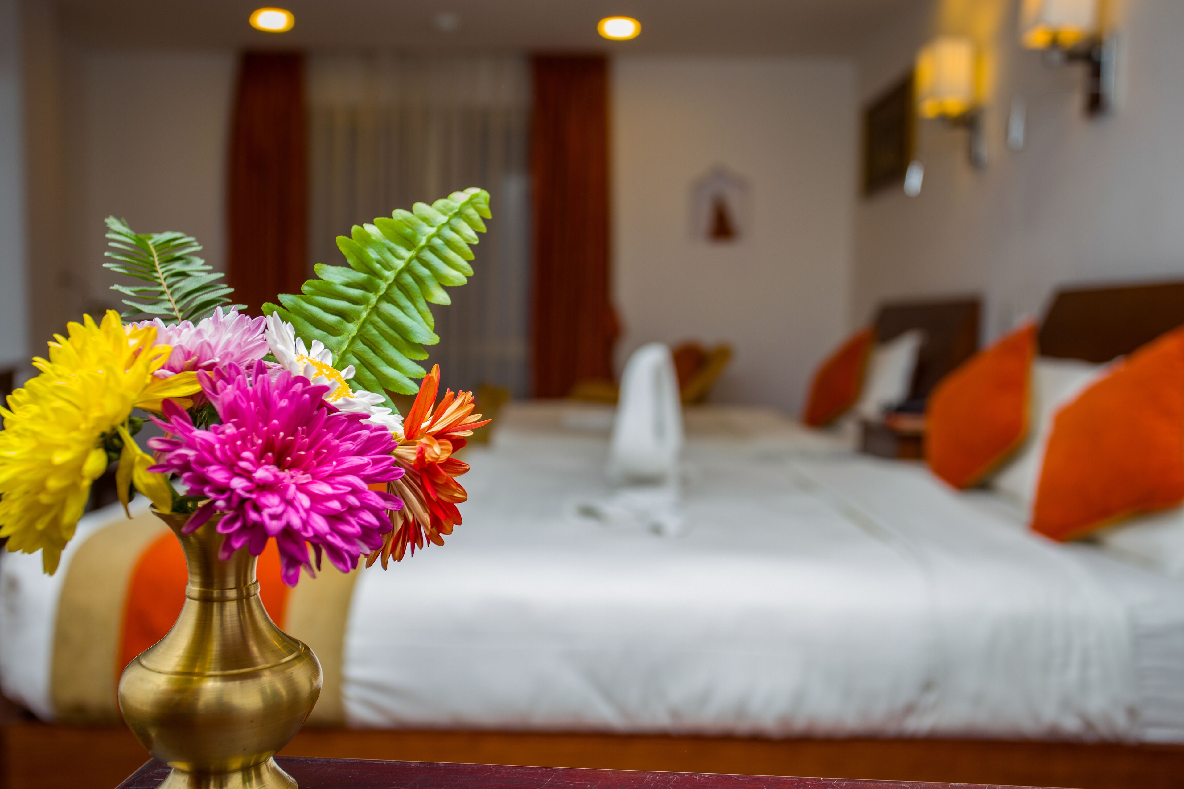 Una habitación de hotel con una cama, almohadas y un jarrón de flores sobre una mesa.