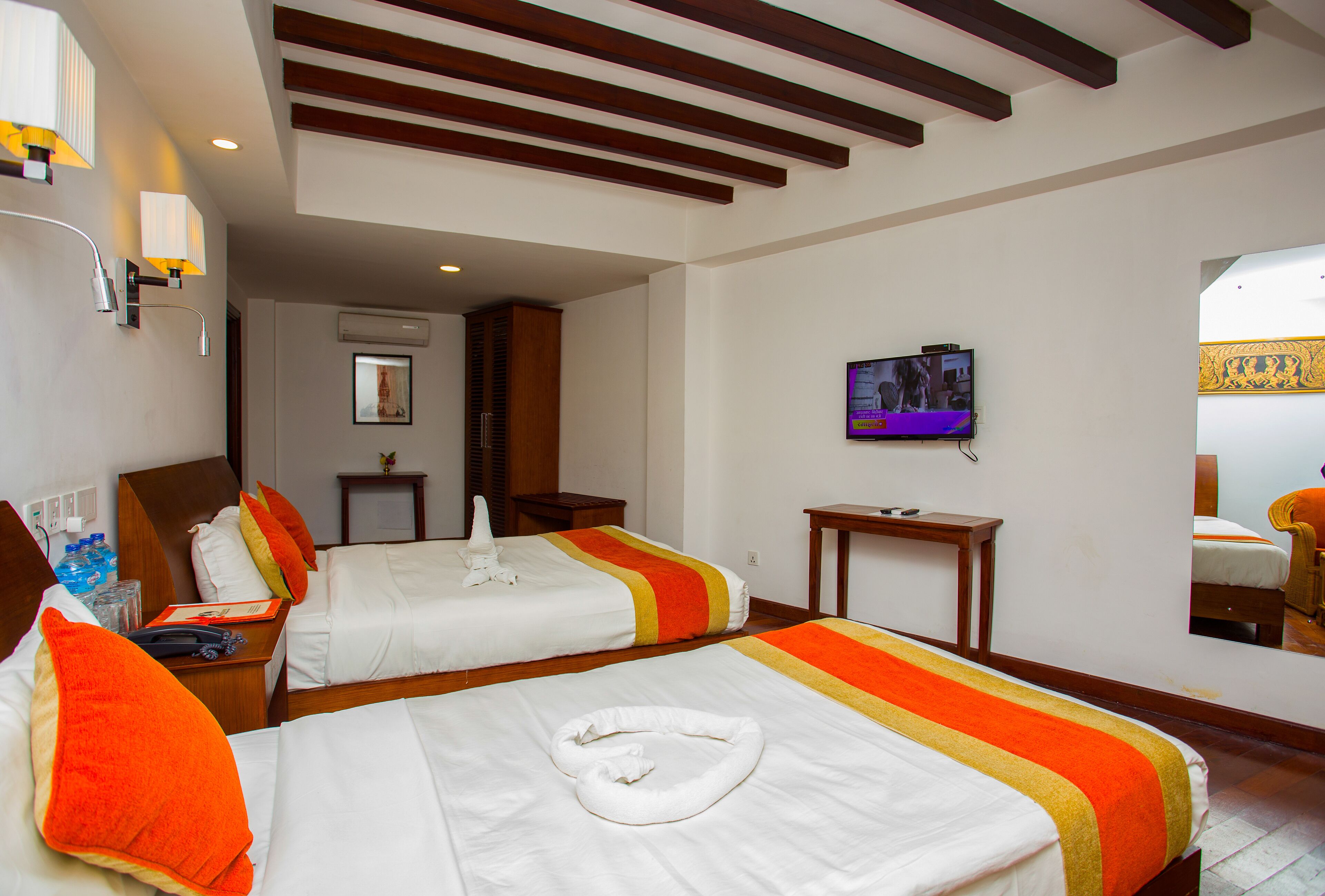 A hotel room with two beds, a TV, a mirror, and a bathroom visible in the background.