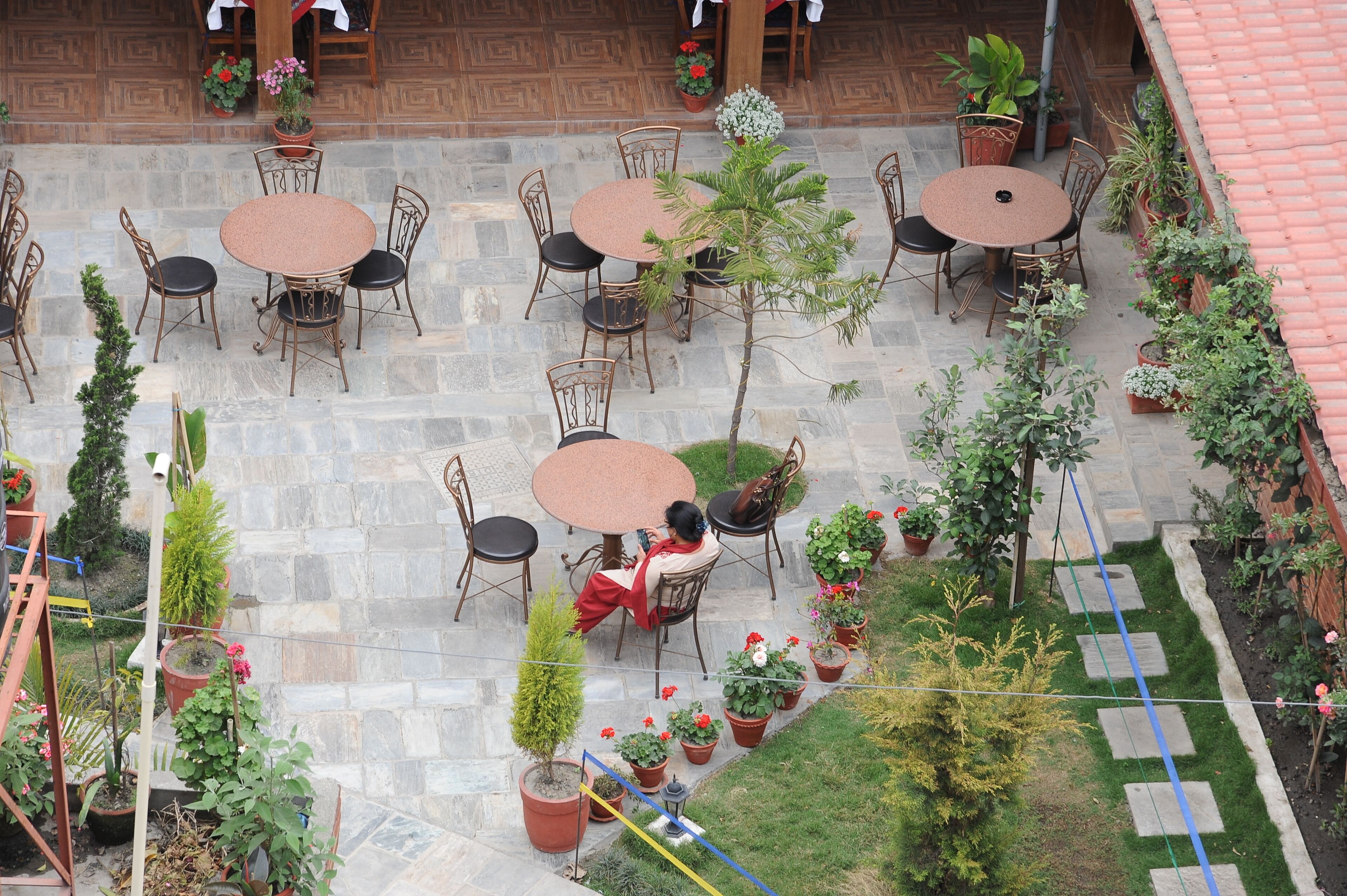 Une terrasse extérieure dotée de plusieurs tables et chaises rondes, entourée de plantes en pot et recouverte d’un sol en pierre.