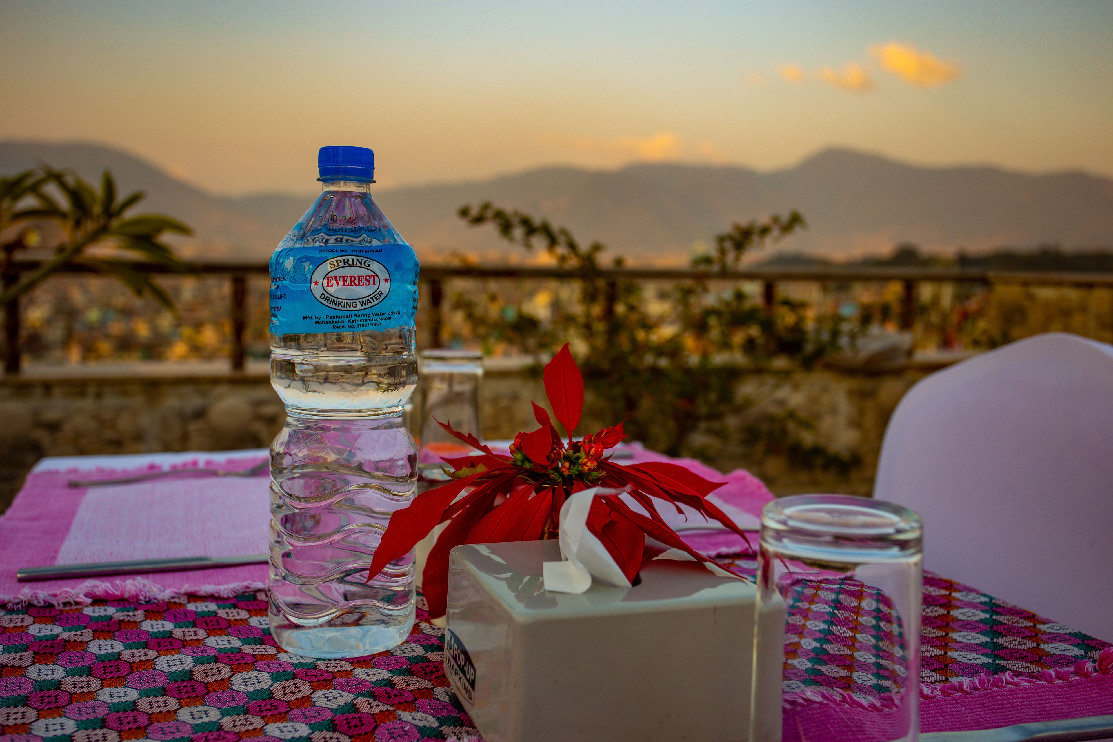 A table with a water bottle, a box, and a glass on a patterned tablecloth.