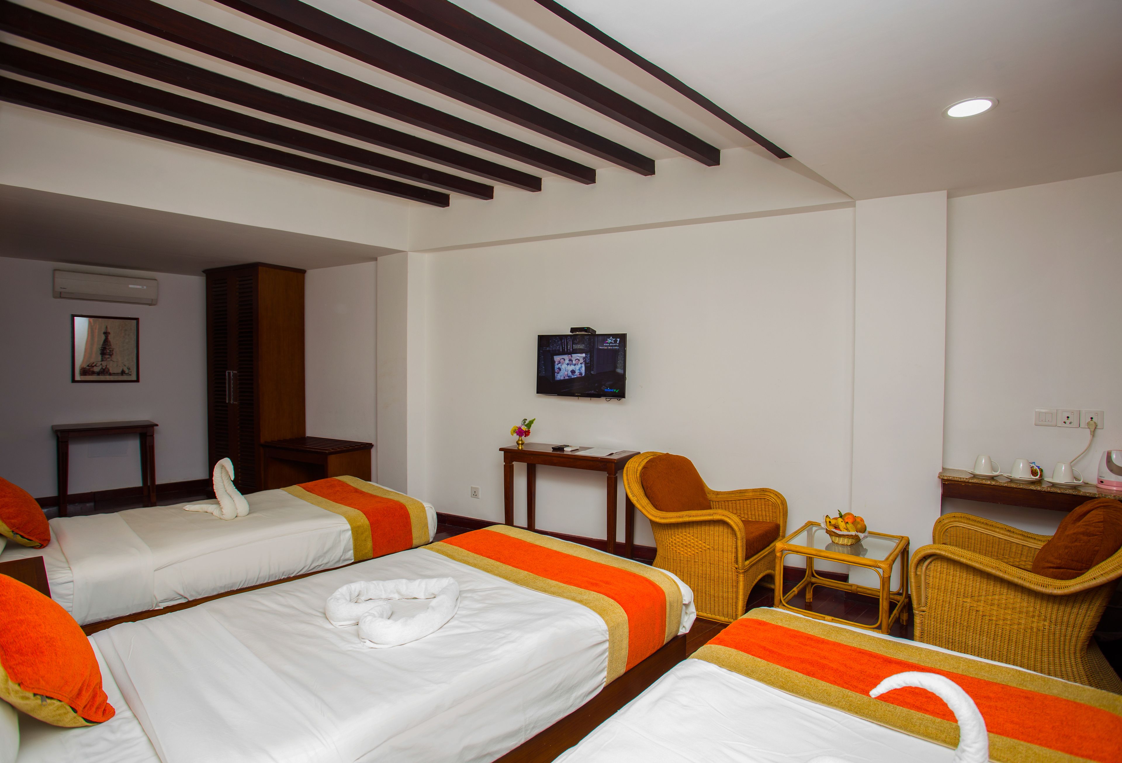 Habitación de hotel con dos camas, televisión, una mesita y sillas de mimbre.
