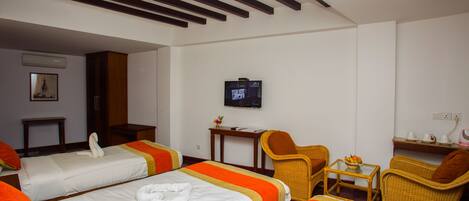 Habitación de hotel con dos camas, televisión, una mesita y sillas de mimbre.