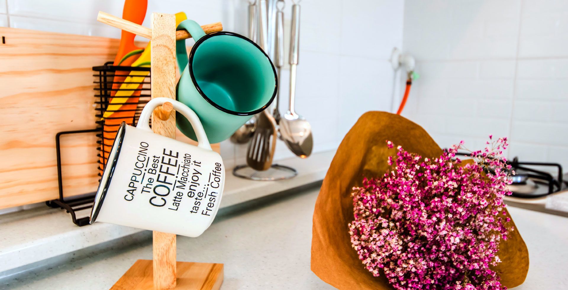 A kitchen counter with a coffee mug, a coffee cup, and a wooden stand holding a coffee mug.
