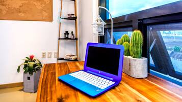 Um laptop sobre uma mesa de madeira, com vista para uma janela, uma planta cacto e um mapa-múndi na parede.