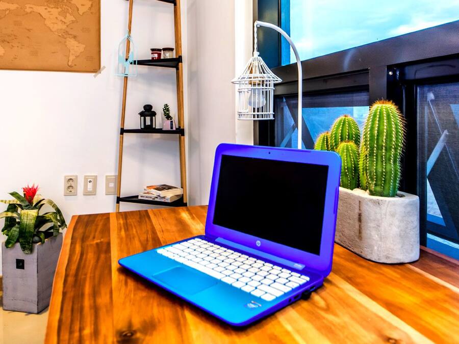 Um laptop sobre uma mesa de madeira, com vista para uma janela, uma planta cacto e um mapa-múndi na parede.