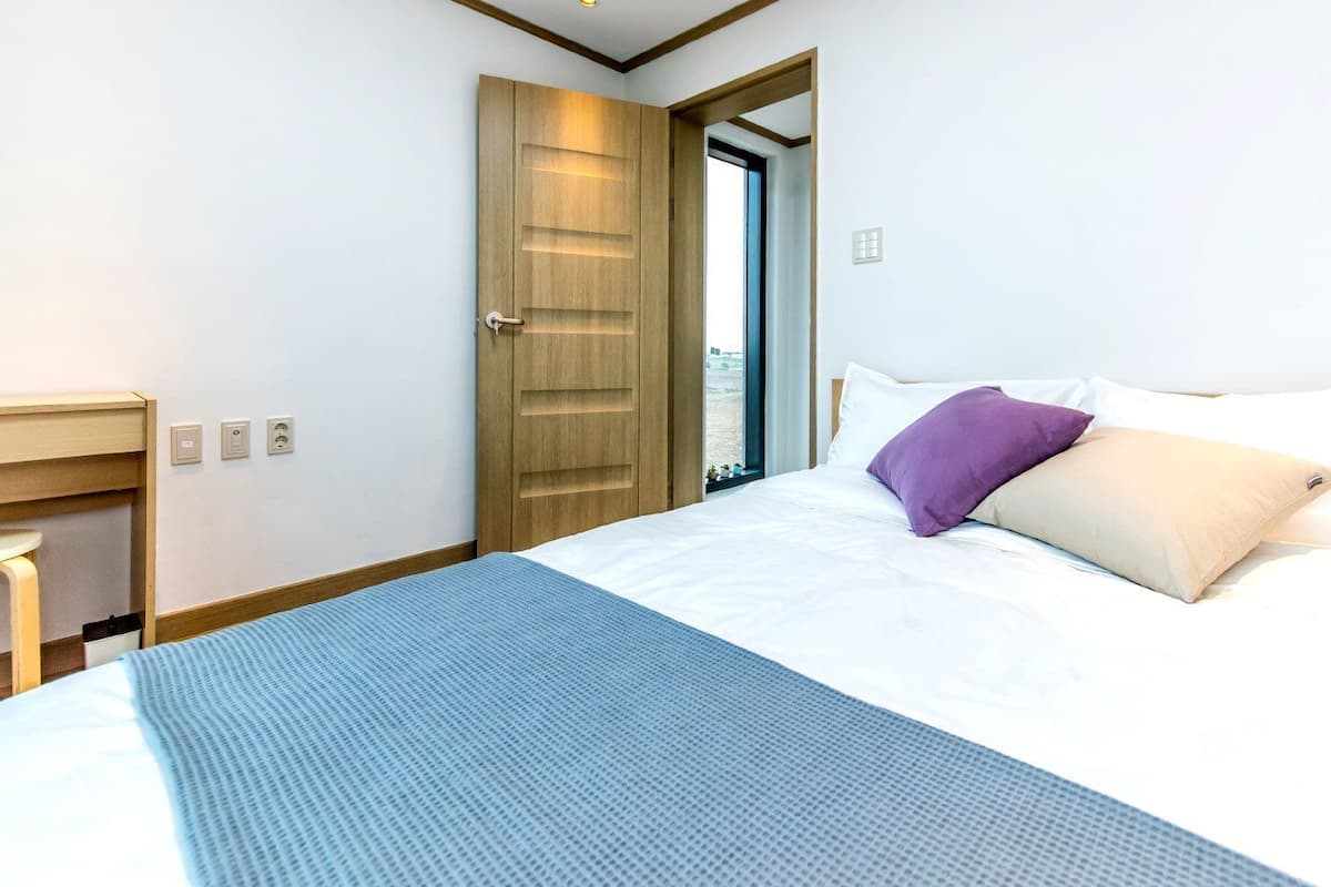 A hotel room with a bed, a desk, and a door.
