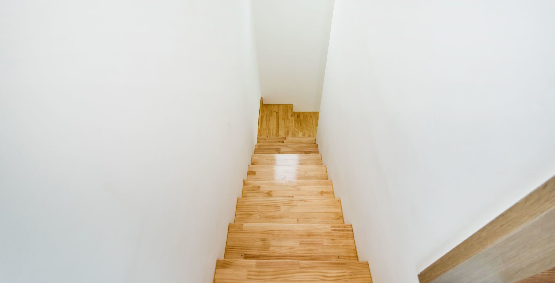 A narrow, wooden staircase with white walls, leading to a higher floor.