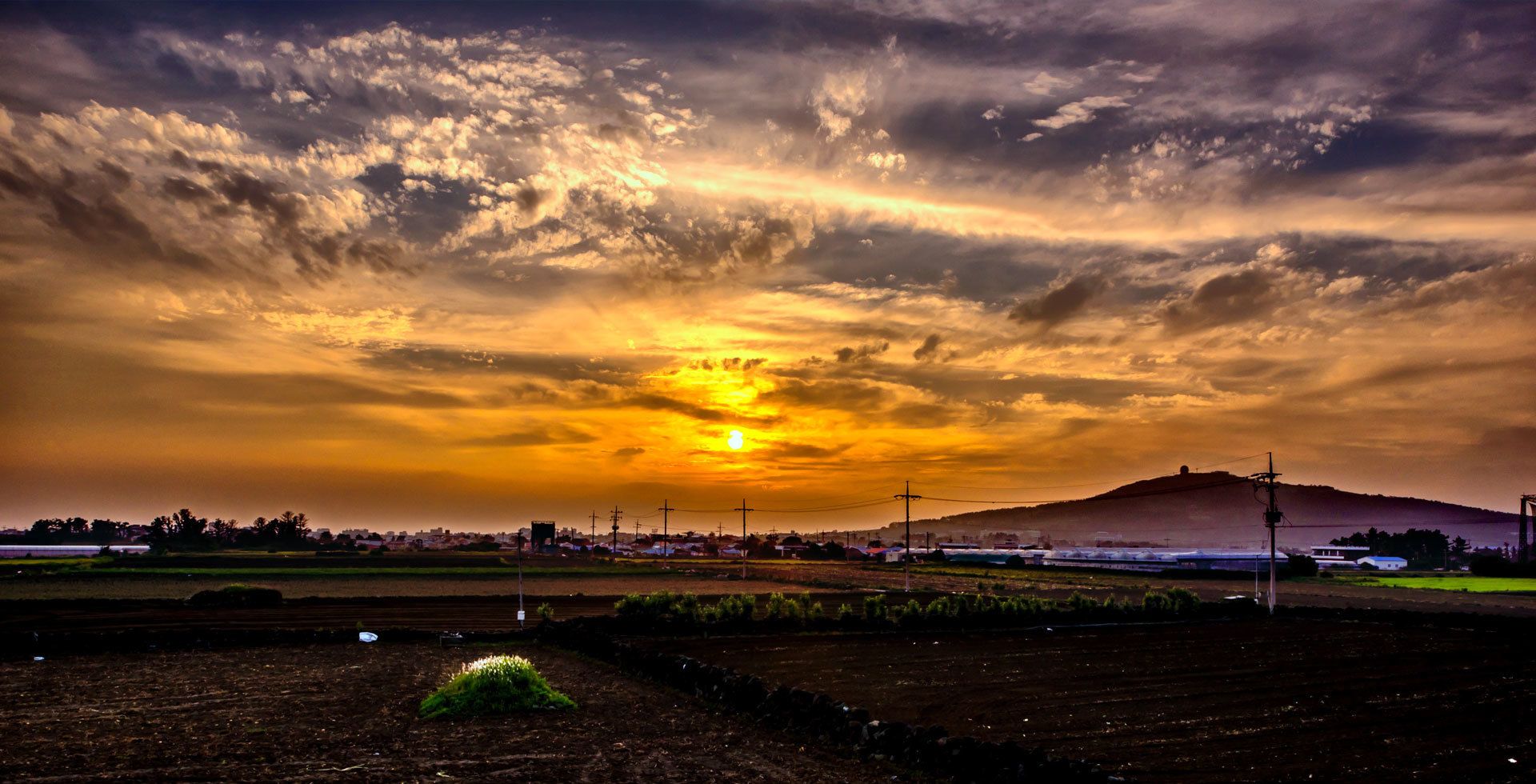 A sunset over a rural landscape with fields and a hill in the distance.