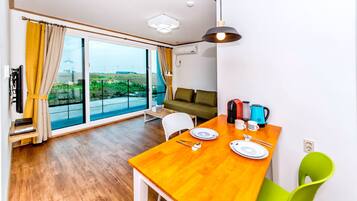 A modern living room with a wooden dining table, a sofa, and a large window with curtains.