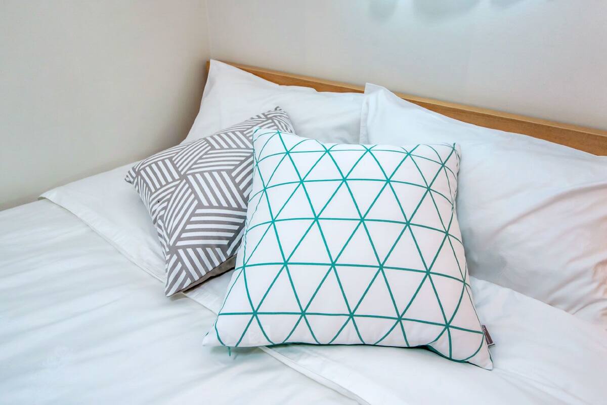 A neatly made bed with white linens and two decorative pillows, one with a geometric pattern and the other with a striped design.