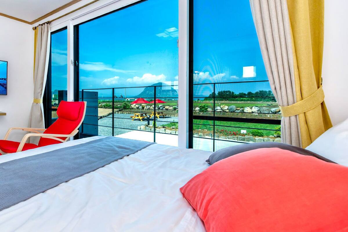 A hotel room with a large bed, a red chair, and a TV on the wall.