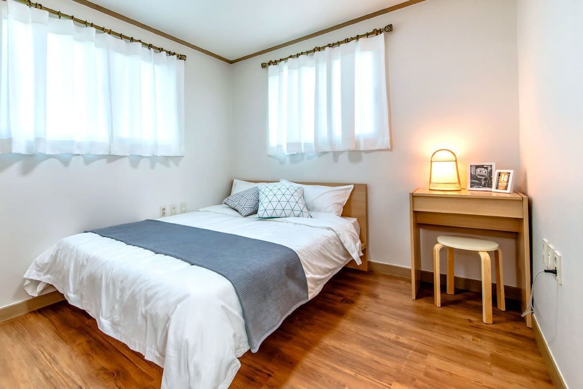 A bedroom with a bed, bedside table, chair, and a desk with a lamp.